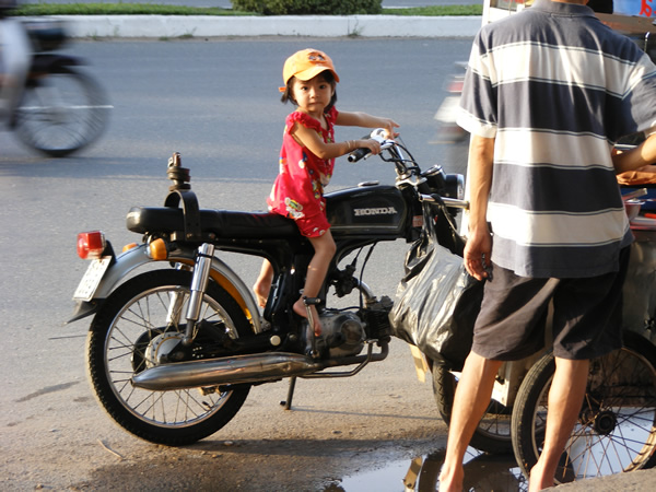 A young girl near her father on parked motorcycle in Ho Chi Minh City.