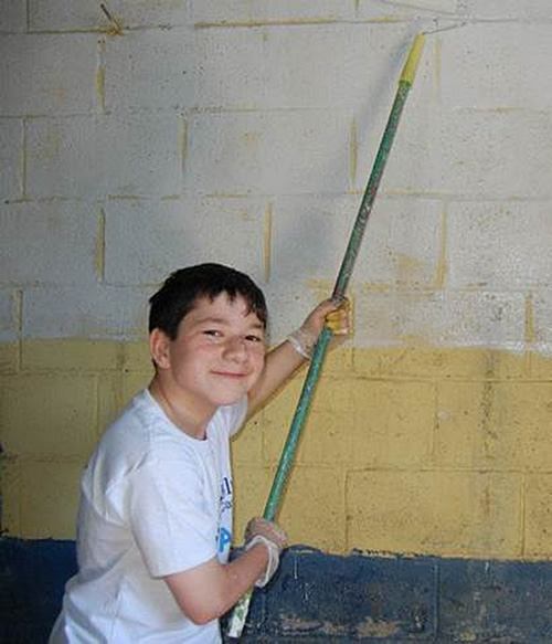 Teen Zach volunteers to paint wall of local school.
