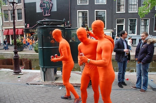 Men in orange waking the streets on Amsterdam along a canal during the festival.