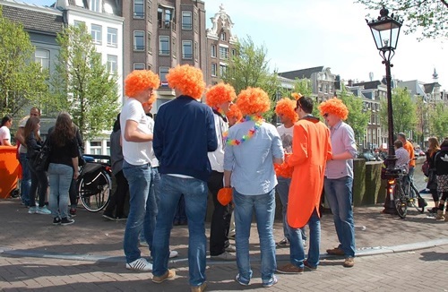 Revelers congregating on a street corner during the Amsterdam festival wearing orange hair.