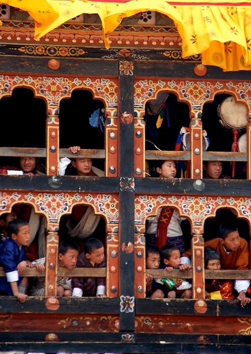 Bhutan children watching the festival from windows of a colorful house.