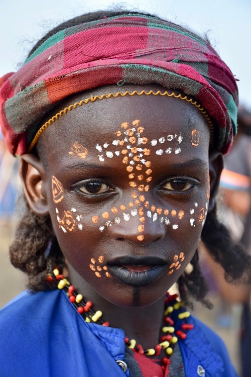 A Wodaabe boy with colorful face paint stares back at the author.