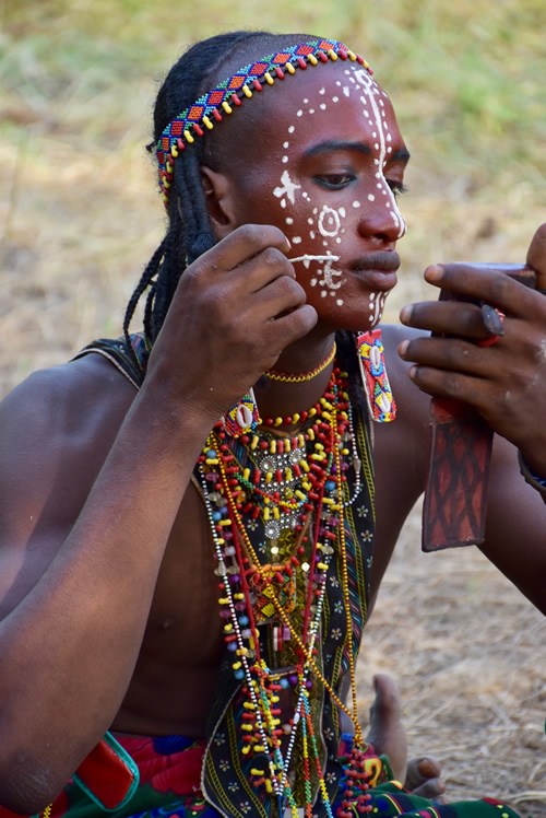 Man applying make-up and wearing many colorful beads, in preparation for the Gerewol Festival performances.
