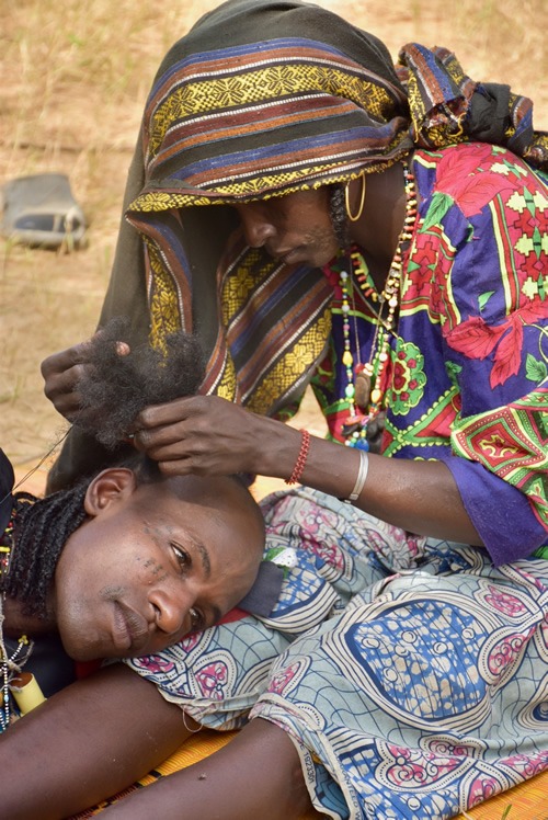 Family member braiding a young man's hair among the Wodaabe in Chad.