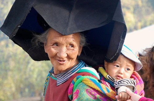 Yi woman with black head dress and child on her back.