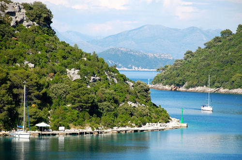 The Croatian coast close to Dubrovnik with sailboats coming back to green but rocky shores.