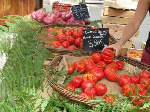 A vendor sells ripe red tomatoes and onions at a market in Europe.