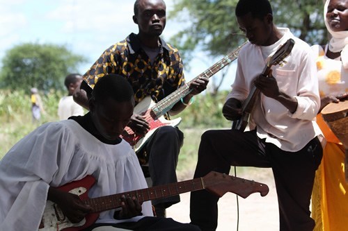 Three musicians playing electric guitar outside in Africa.