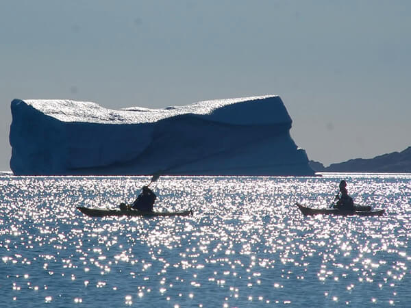 Fellow travelers in paddling boats near a spectacular iceberg in the Arctic.