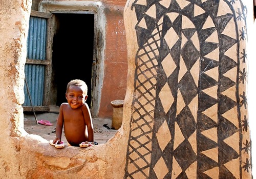 Little boy smiling at his dwelling in Burkino Faso.