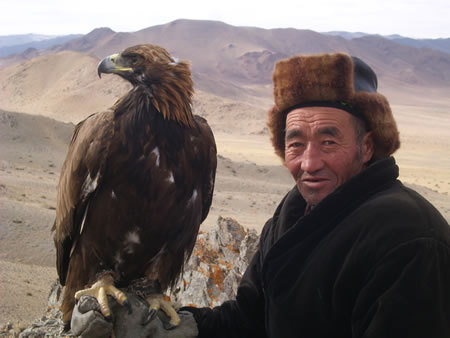 A Kazakh eagle hunter in Mongolia stands holding the bird in his hand.