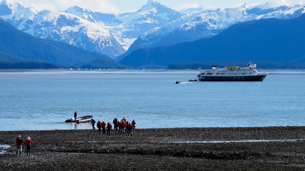Cruise ship in Alaska with people mountain boat to return to the vessel and a mountain backdrop.
