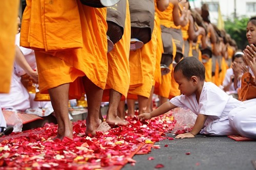 A boy reaching for rose petals during a Buddhist festival in Bangkok.