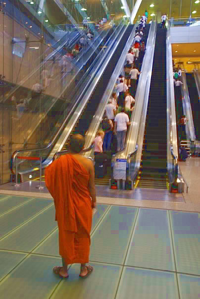 Monk going up escalator in Singapore.