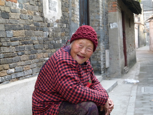 Friendly local woman smiling as she sits on a curbside in a Chinese town.