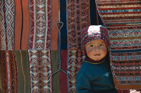Peruvian child peeking out from textiles.