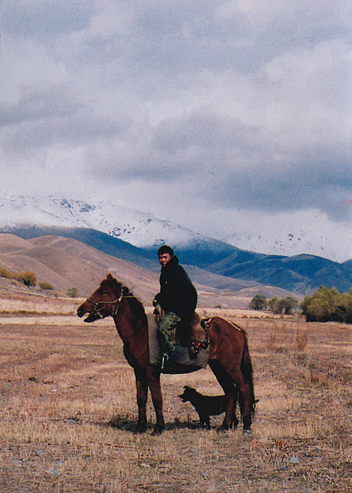 Kyrgyzstan man on horse with dog.