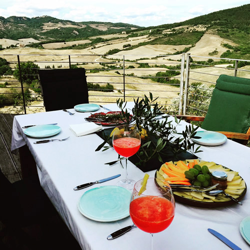 A meal is soon to be served on an outside deck overlooking  Tuscan fields and hills.