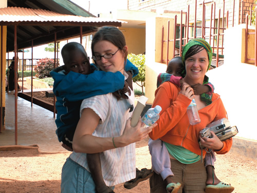 Student volunteer service learning abroad with two women carrying two children on their backs.