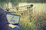 Teaching English online, teaching on laptop outside in front of pond.