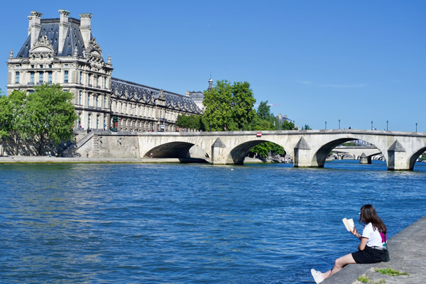 A woman reading a book on the banks of the Seine in Paris, France