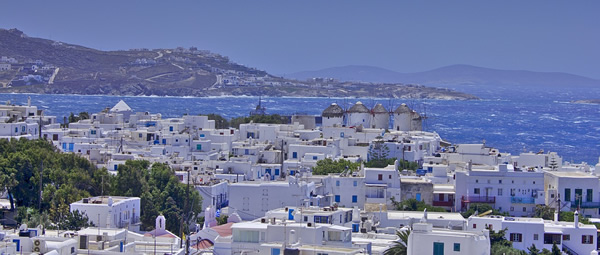 The iconic painted white and blue houses of Mykonos, Greece with the blue seas in the background.