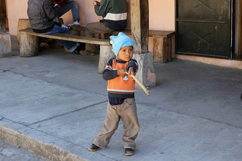 A child in Ecuador playing an imaginary game on the sidewalk with a magic stick.