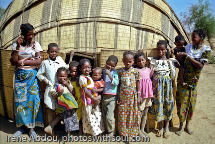 Fulani family standing in front of grass mat house