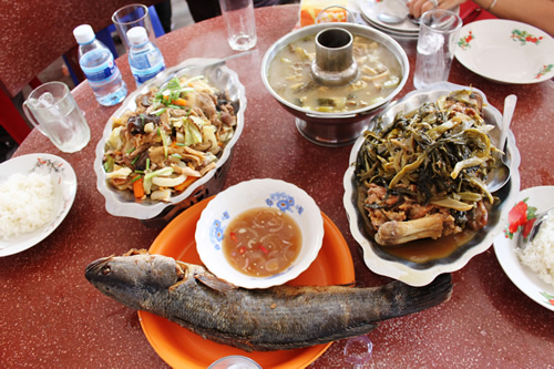 A sample Cambodian meal with a large fish and side dishes of noodles with vegetables and red curry sauce.