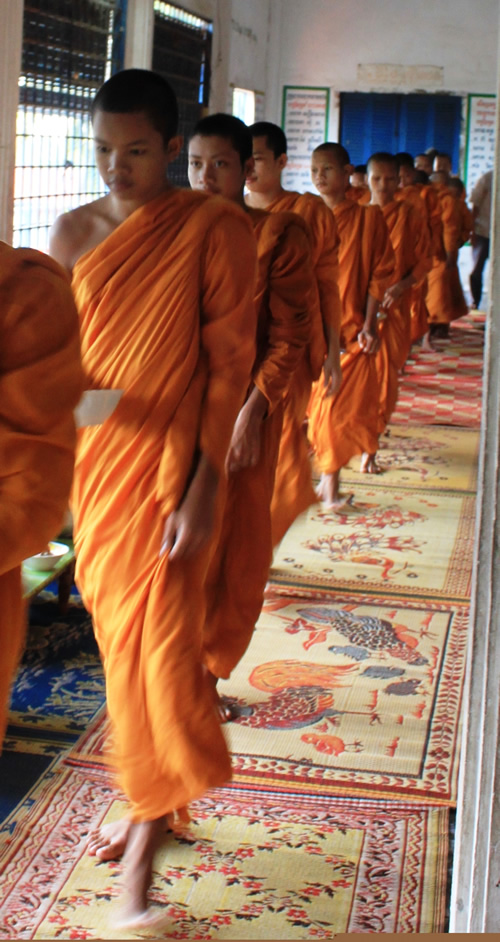 Buddhist teens in orange walking on carpets during a ceremony.