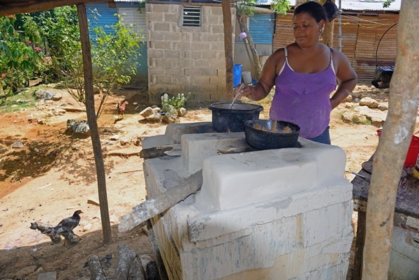 A woman cooking lunch outdoors, over an open fire hearth.