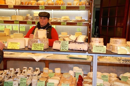 Cheese shop with many Franch cheeses, with a woman serving, in Paris.