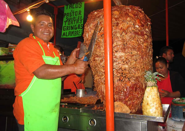 Cheap Mexican pork tacos, with a man cutting the succulent meat.