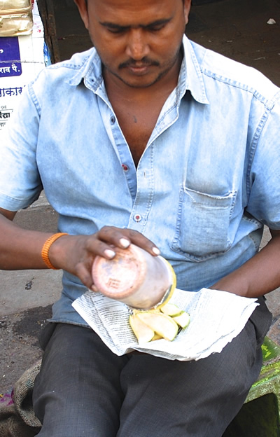 A street vendor selling green mango strips, wrapped in a newspaper