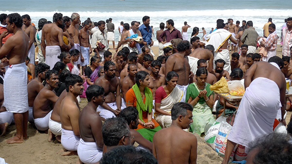 People in white towels and clothes on the beach for ceremonies.