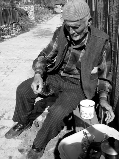 Turkish elderly man holding a small glass cup of tea.