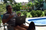 Teaching English online, teaching on laptop outside in front of pool.