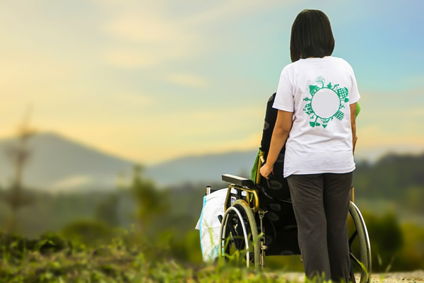 A woman working as a caregiver in the UK, pushing a wheelchair in the woods.