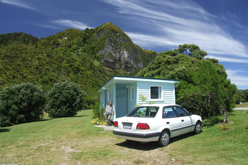 Living in holiday park in New Zealand with their car in front of a small house.