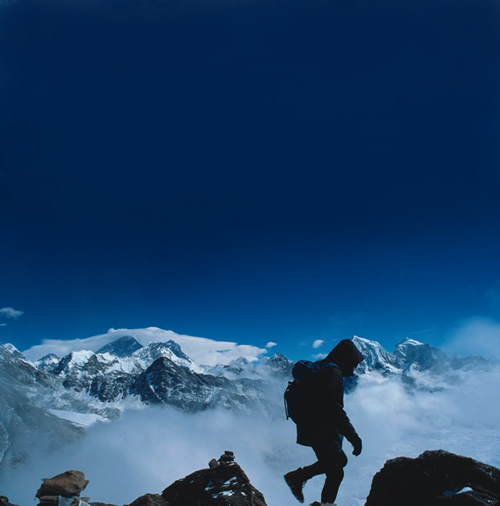 A trekker climbing the mountaintop in Nepal with the snow-capped Himalayas in the background.
