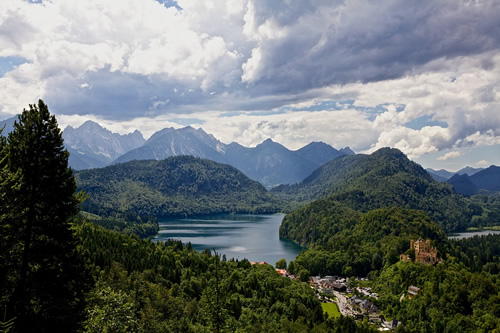 View of the Bavarian alps with green hills and mountains around a lake.